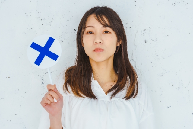 バツ印を手に持つ女性